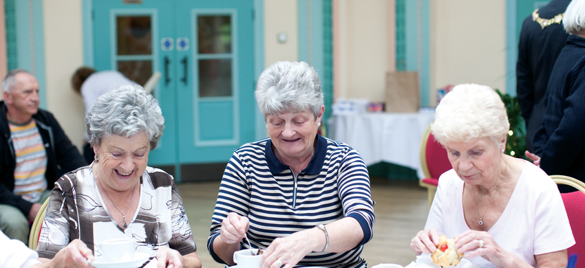 Three ladies sitting at a table enjoying tea and cake