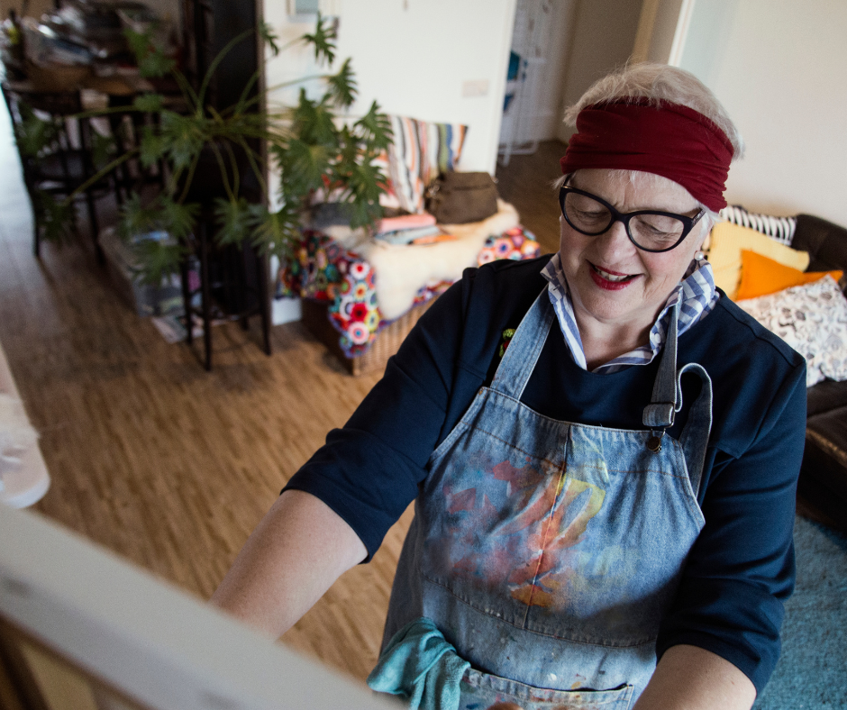 Older woman with paint overalls painting as a way to boost their brain. Boost your brain with ACWG.