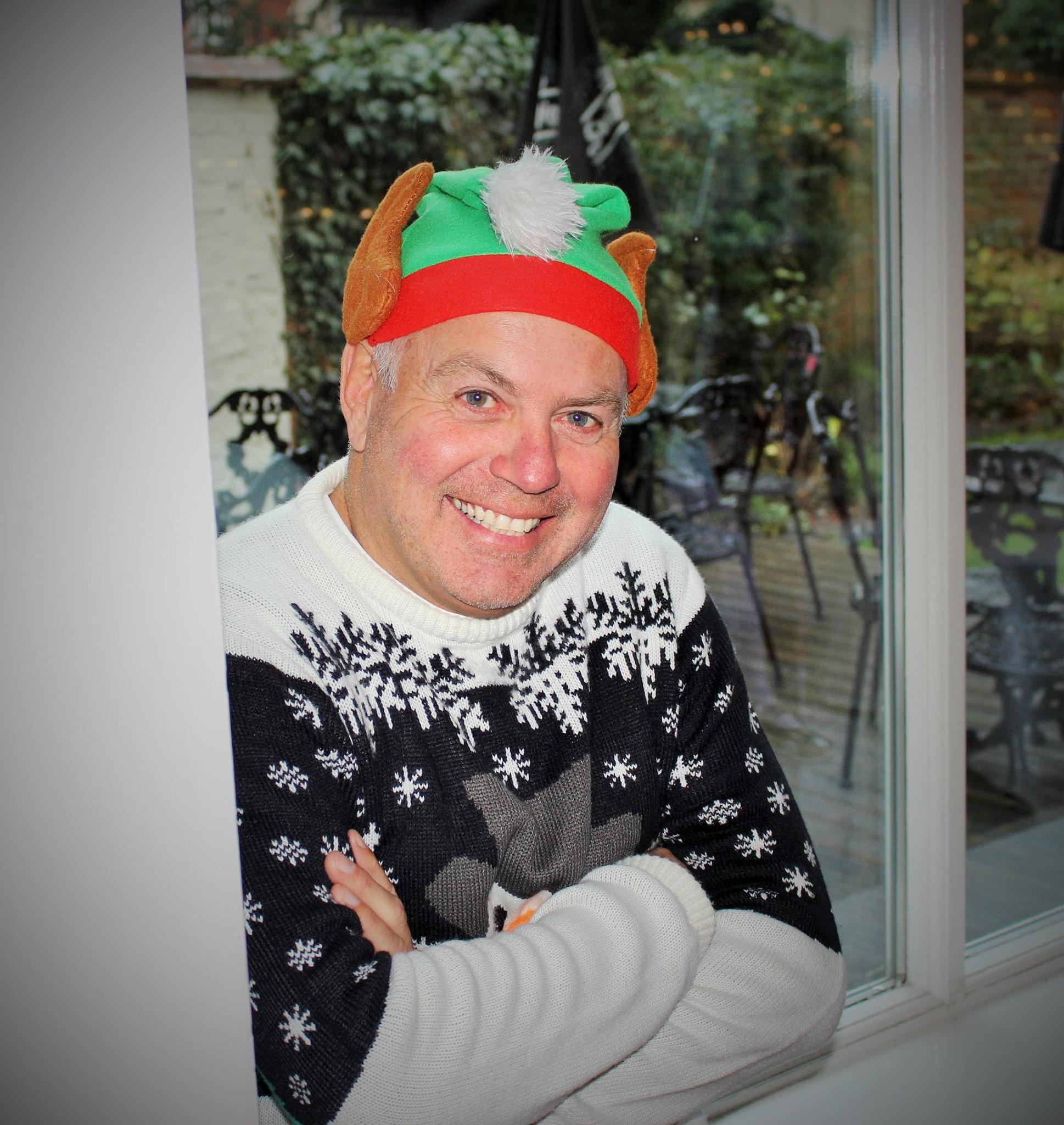 An older man smiling at the camera, wearing a Christmas jumper and a festive 'turkey' hat