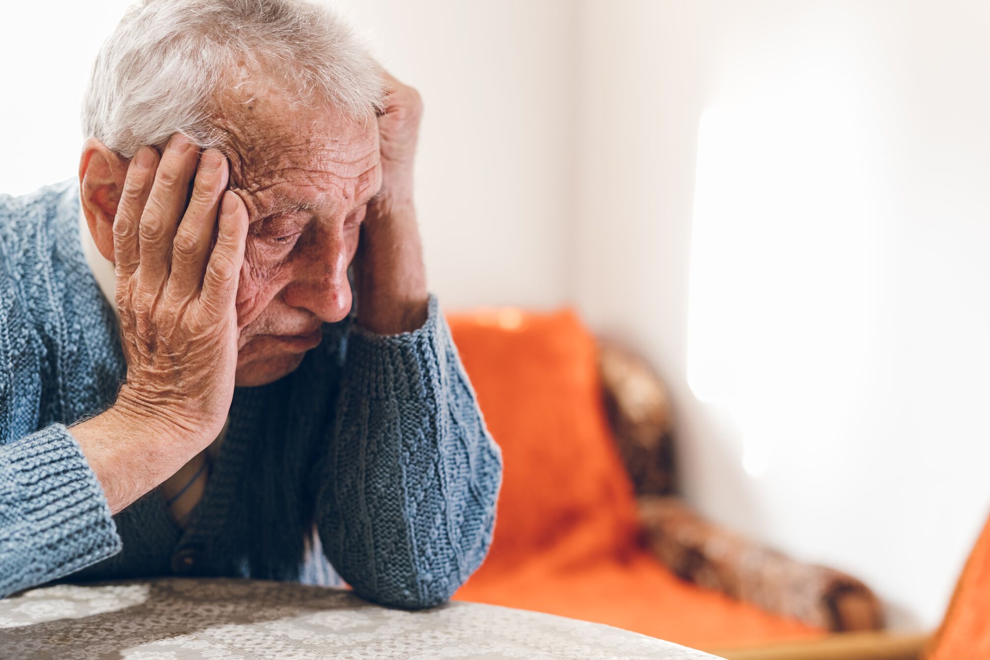 Older man at a table holding his head in his hands in frustration