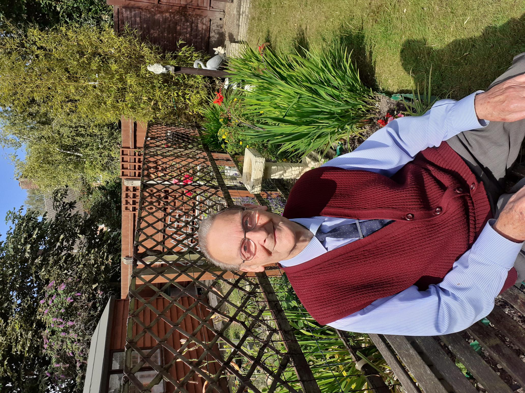 Bryan, an older gentleman sitting on a bench in his garden, smiling at the camera.