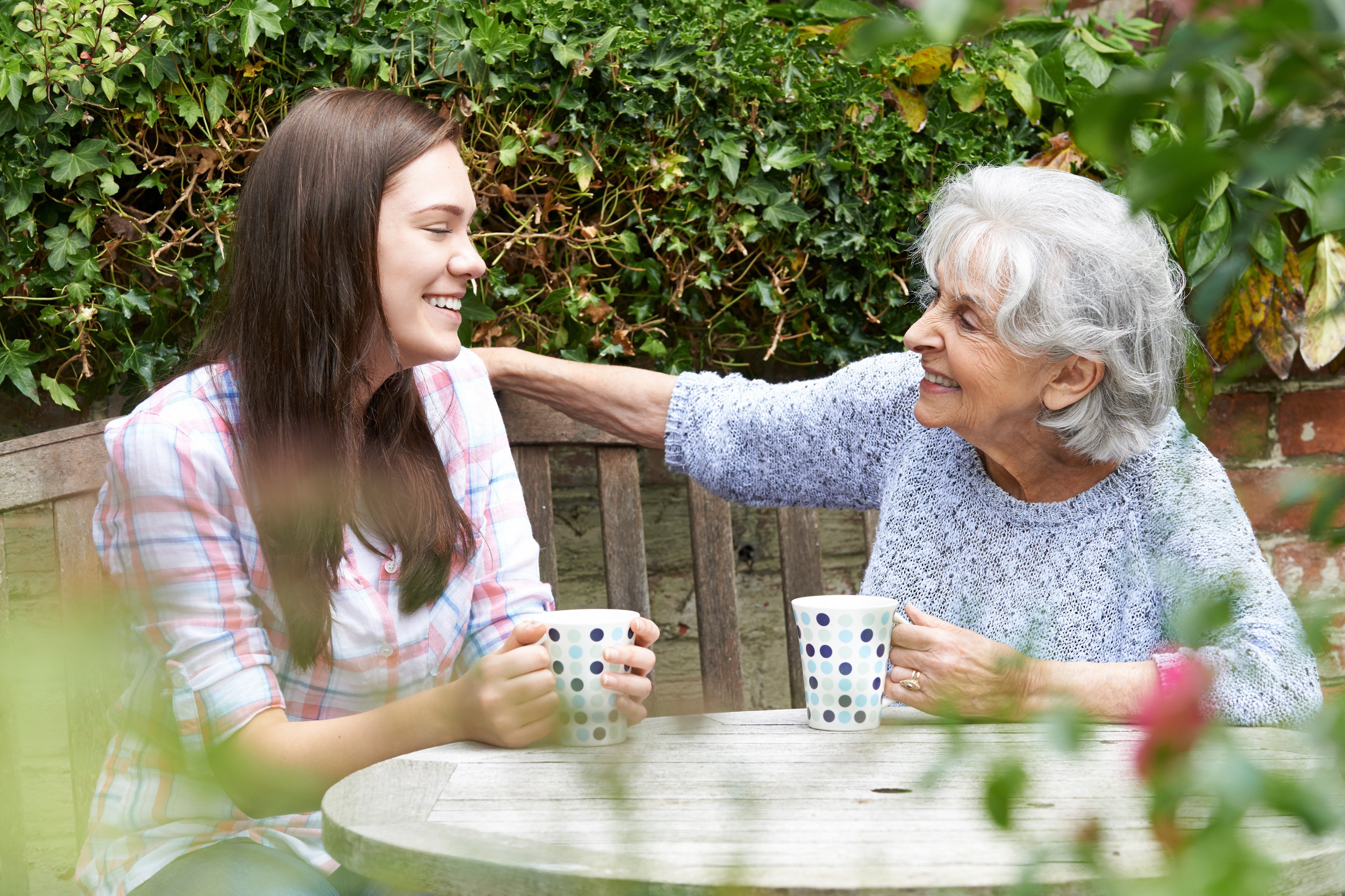 An image of an older woman placing her hand on a younger woman's shoulder and smiling.