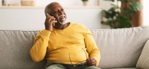 Man on phone wearing a yellow jumper, sat on a sofa.