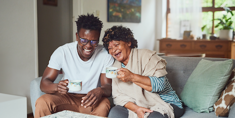 A young black man and older black woman share a laugh while drinking a cup of tea