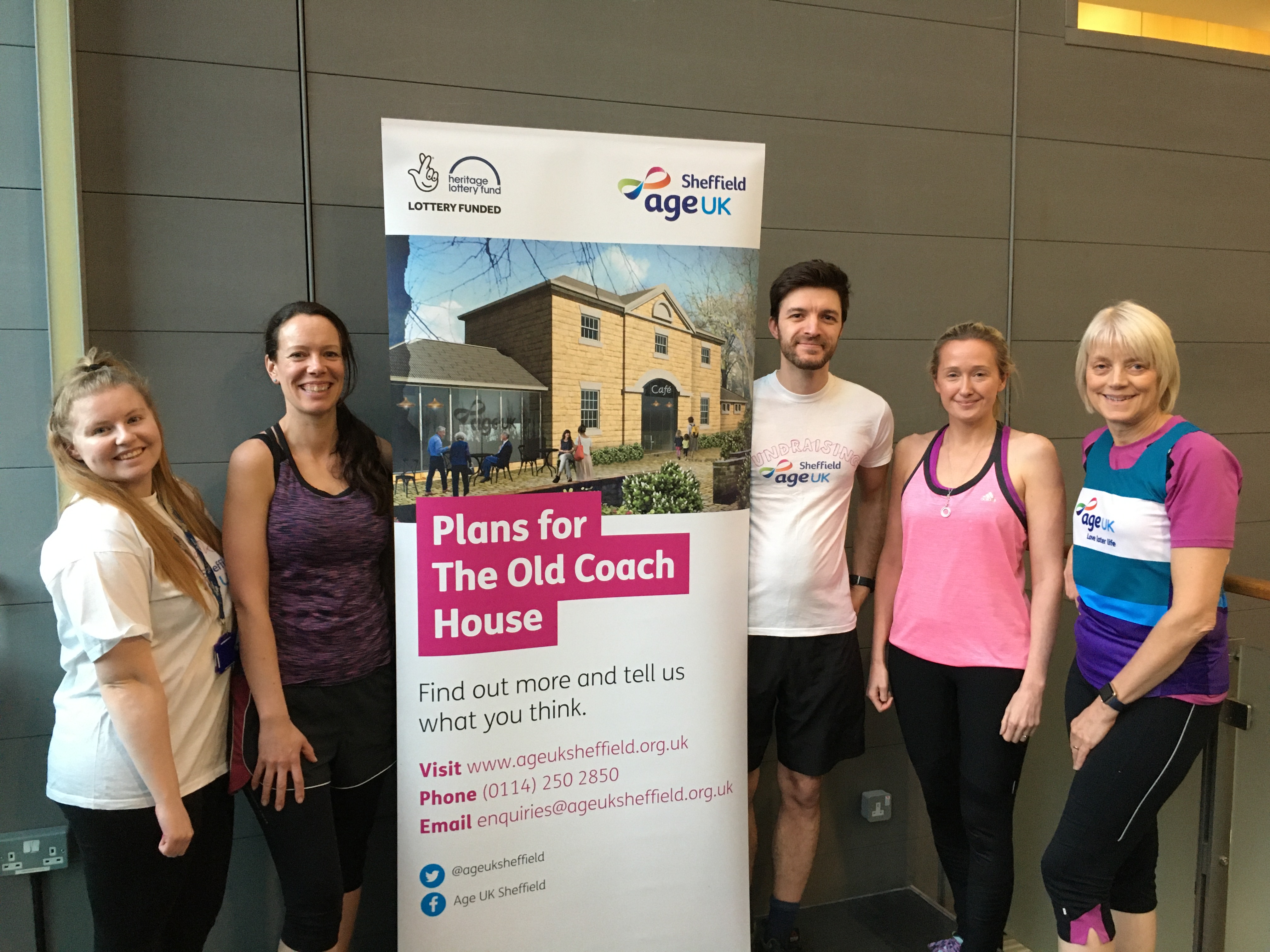 Staff Members pose in running clothes next to a banner advertising the charity's Coach House Project