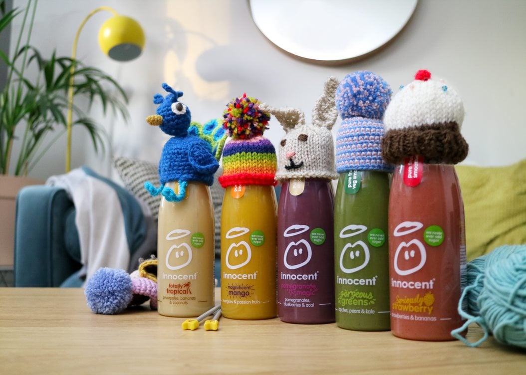 Image shows 5 different innocent smoothie bottles, each with different creative knitted hats