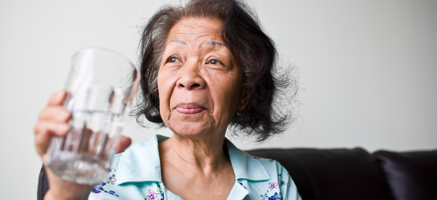 older lady drinking a glass of water in her home