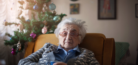 Older woman on sofa alone Christmas tree in background