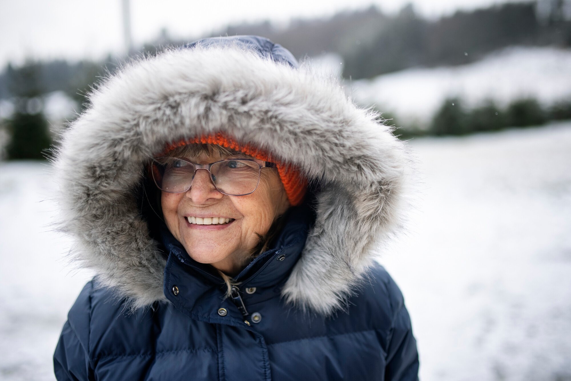 Older woman with coat and hood up with wintery scene in background