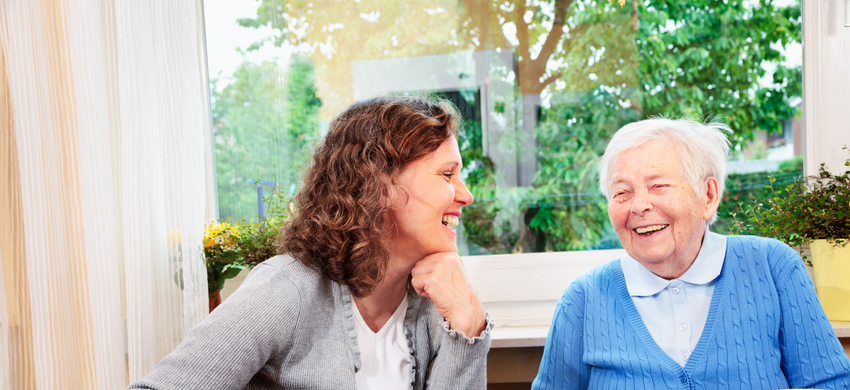 Older lady and younger woman sitting inside smiling