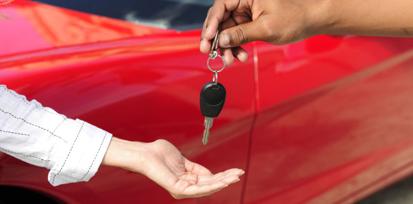 Two people exchanging a set of car keys in front of an out-of-focus red car in the background