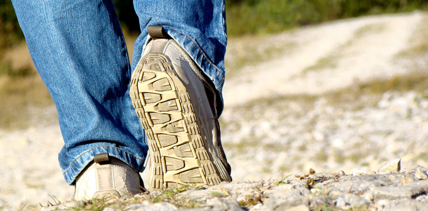 A close-up of someone wearing walking shoes over rocky terrain