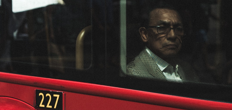 An older man in the window of a red London bus