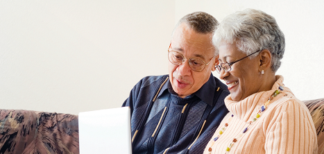 An older couple look at their laptop on the sofa.