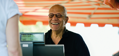 An older gentleman smiles while operating a till.