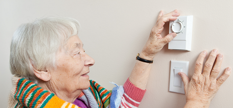 An older lady adjusts her thermostat.