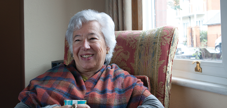 An older woman sits happily in her flat.