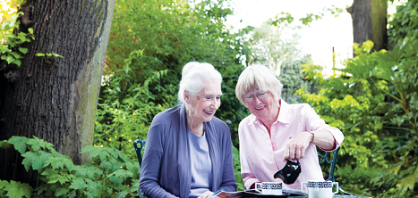 Two women share a pot of tea outdoors.