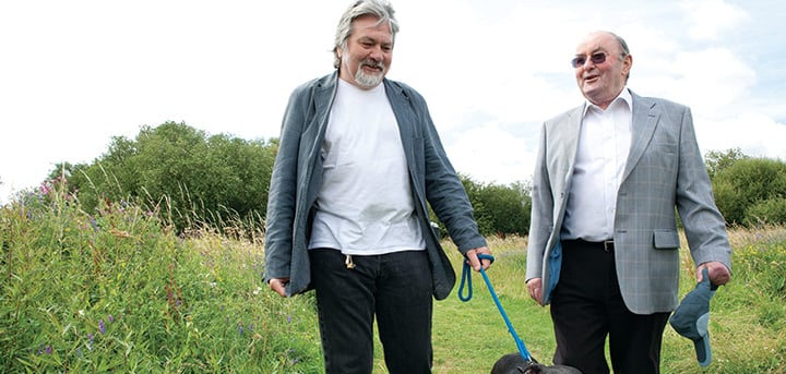 Two men walking a dog in a park