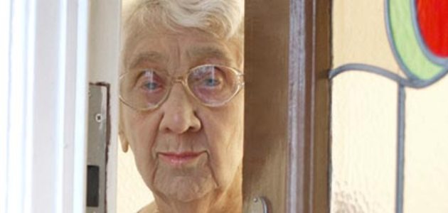 Older lady looking through gap in front door