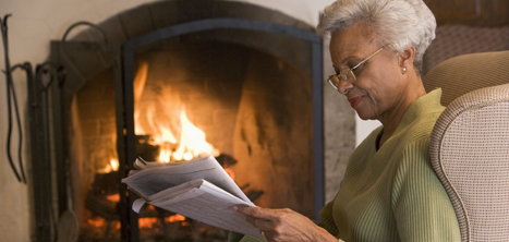 Older woman reading the paper by a fireside
