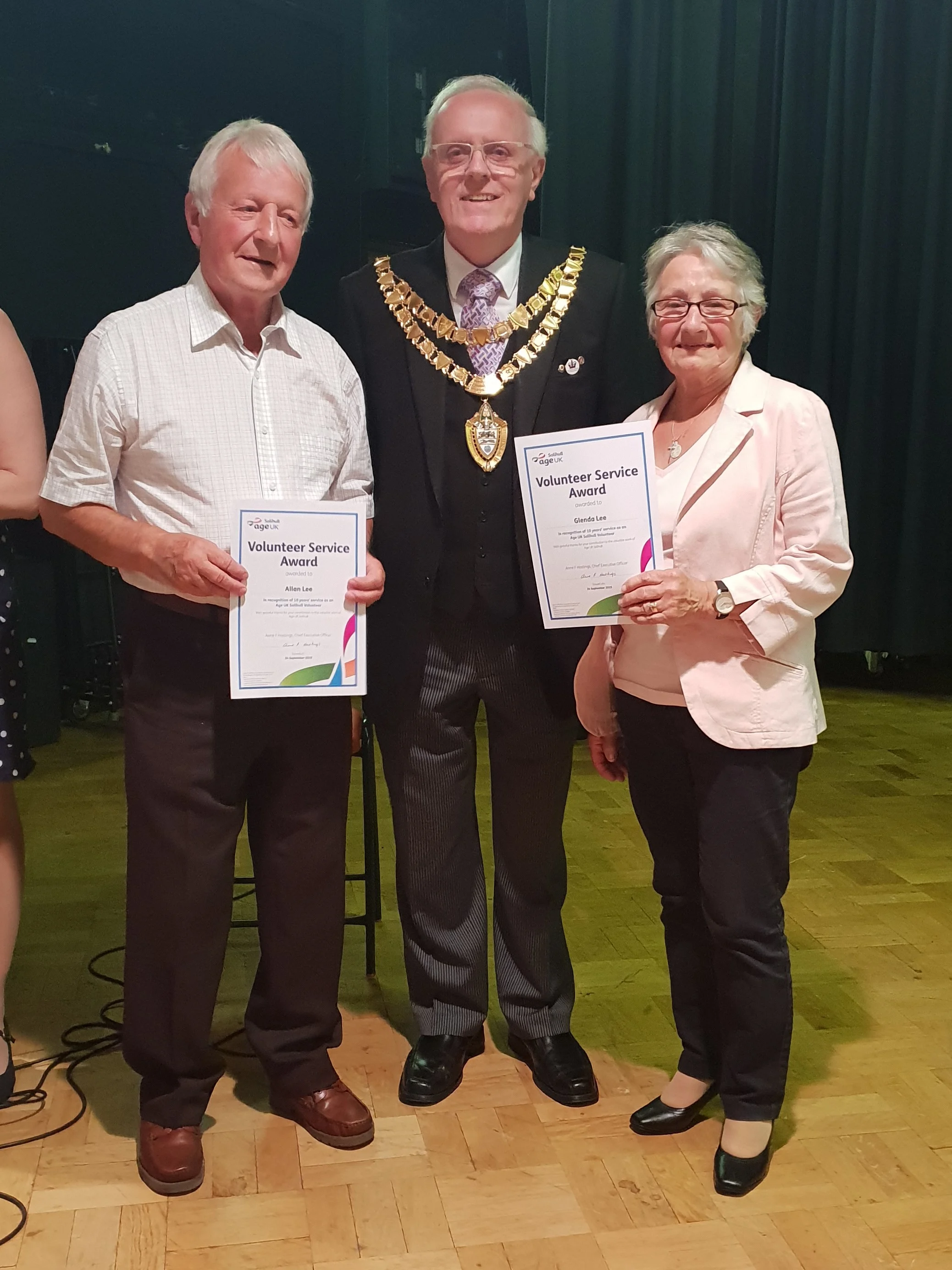 Two people standing next either side of the Mayor of Solihull, holding certificates to mark 10 years' volunteering for Age UK Solihull