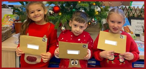 Three children stood in front of a Christmas tree, holding envelopes containing Christmas Cards