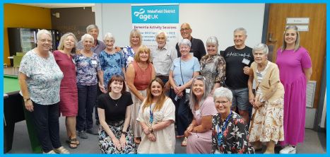 Group of people who are all taking part in the Age UK Wakefield District Dementia activity session. Smiling and looking at the camera