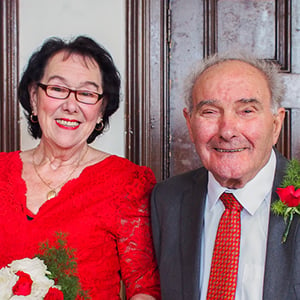 A man and woman smile at a wedding in smart clothes