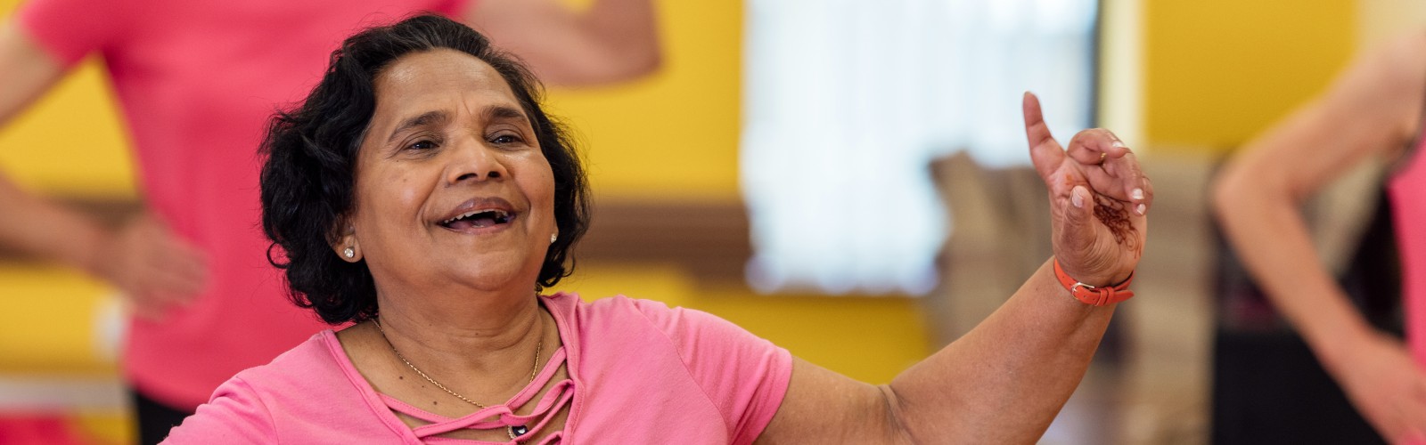 An older woman in a pink t-shirt dances happily