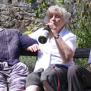 A woman sits on a bench and jokingly drinks from a bottle of champagne