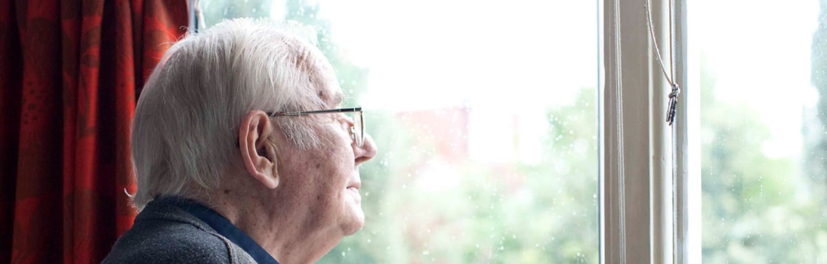 An older man, wearing glasses, looking out of the window