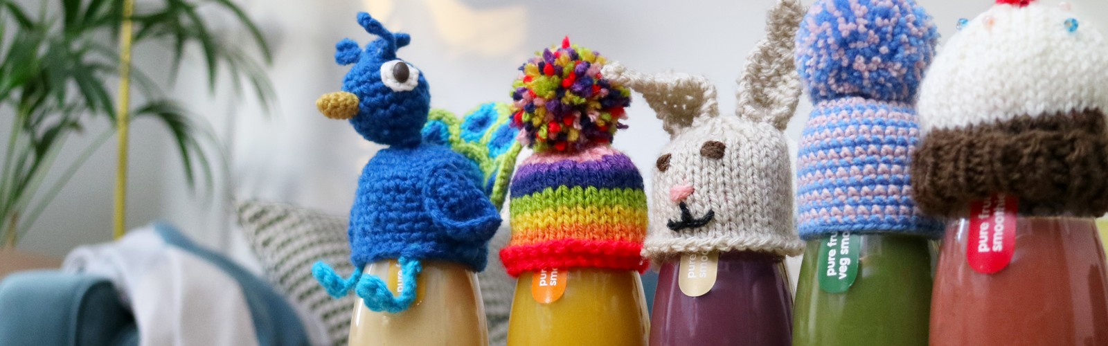 A line of small knitted hats on top of innocent smoothie bottles.