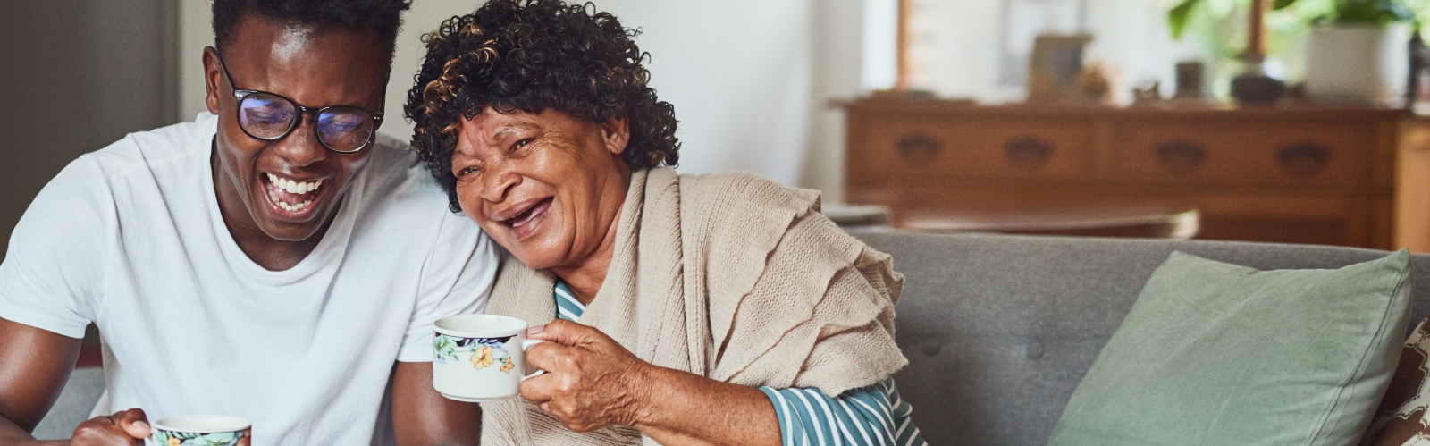 A young man laughs with his grandmother while drinking tea
