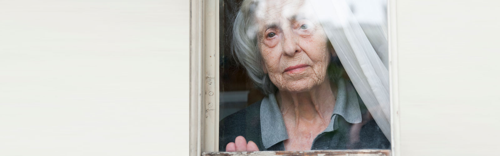An older lady sits in her kitchen, looking worried