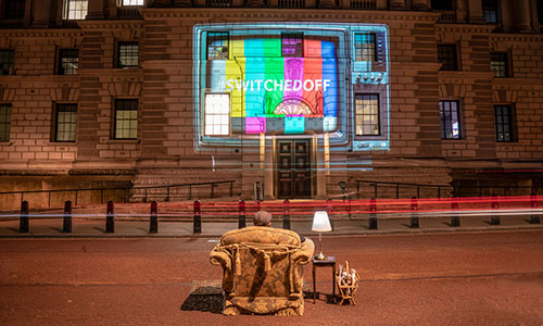 A man watches a projected image of a television set on the side of a building