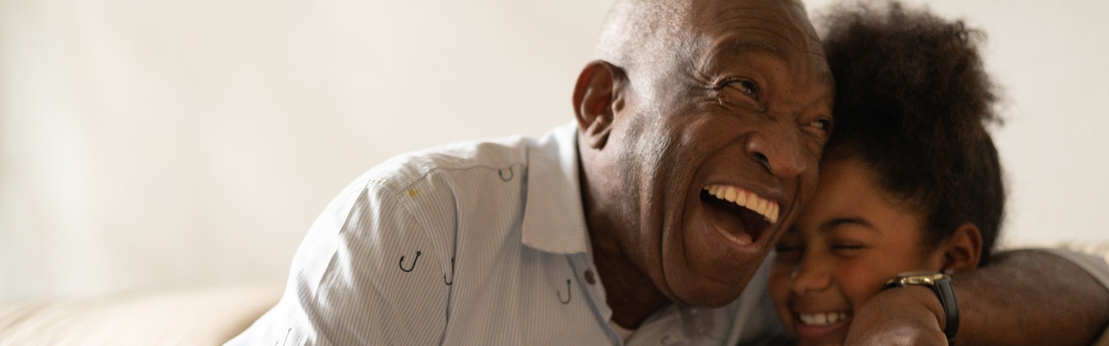 A Black older man laughing and hugging his granddaughter 