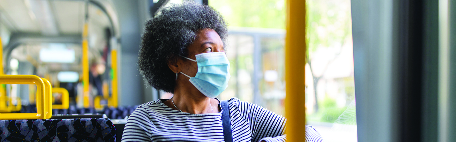 An older woman sits on a bus wearing a face covering