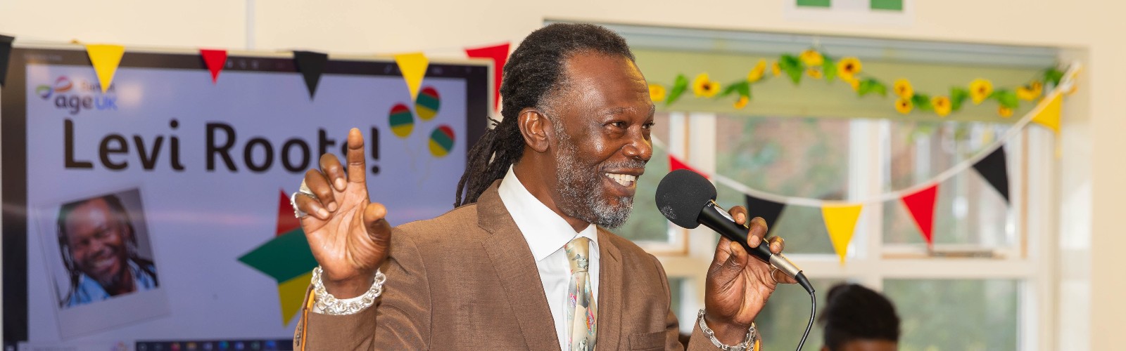 Levi Roots, smiling and holding a microphone