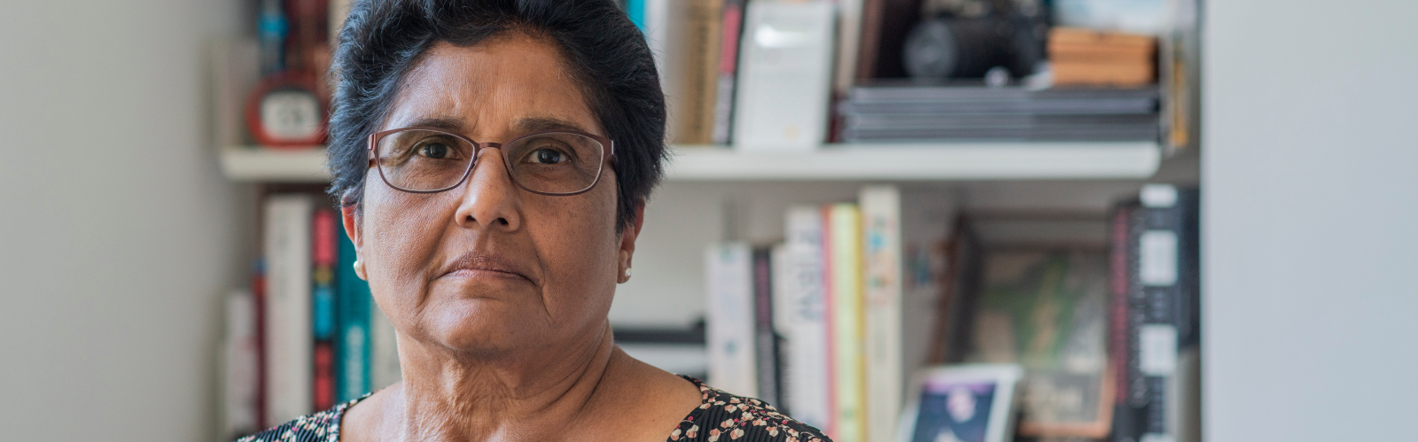 Woman stands in front of bookshelf, looking to camera