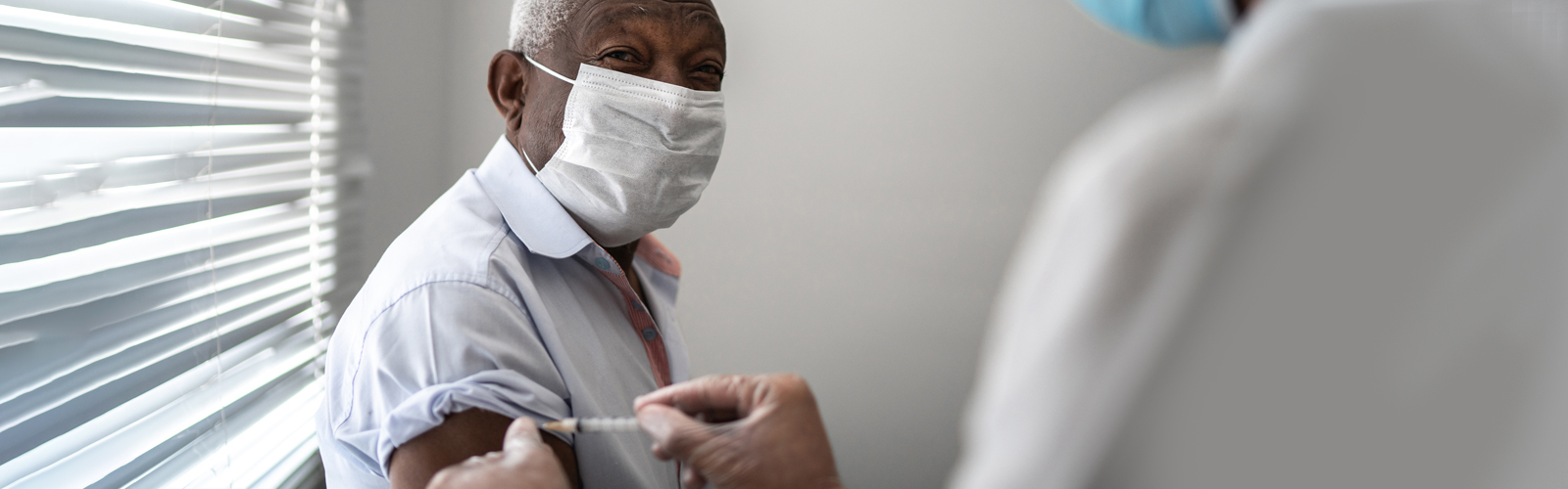 An older man wearing a face mask receives the vaccine