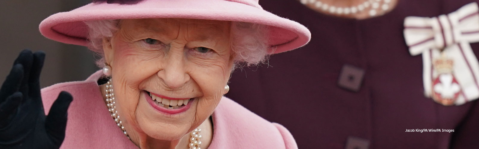 An image of Queen Elizabeth II, dressed in pink, smiling and waving at the camera