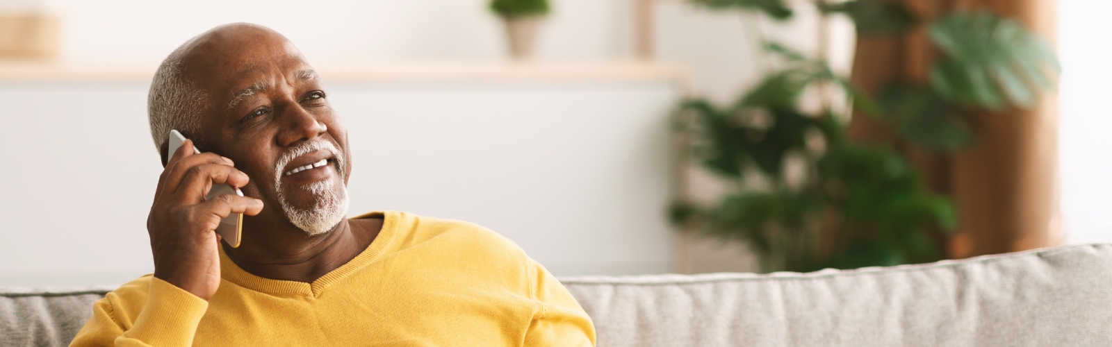 An older Black man sits on a sofa taking a phone call