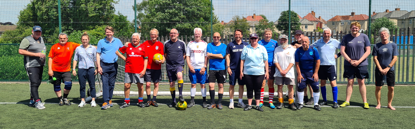 A group of 15-20 older men and women dressed in football kit look at the camera