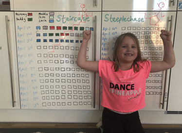 A young girl in a pink top, stood in front of a whiteboard