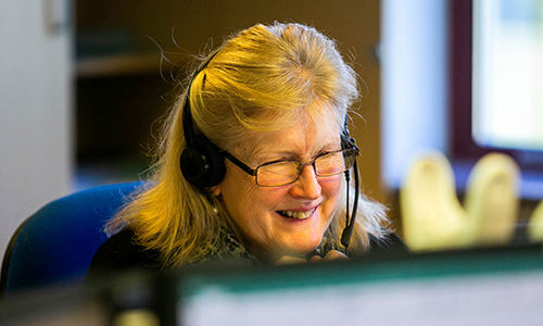 A lady with glasses and a headset speaking to someone on the phone