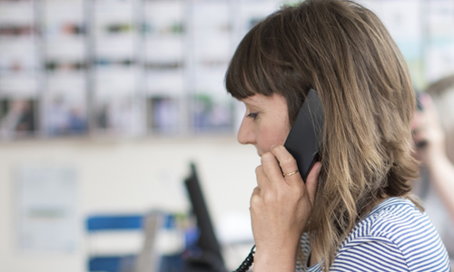 A woman with glasses on a call, sat in front of a computer screen