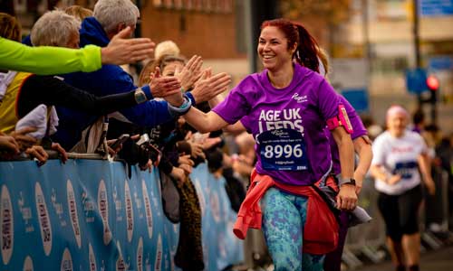 Woman giving high fives to the crowd whilst running in the Age UK Leeds Abbey Dash