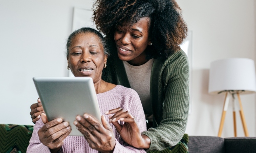 An older woman uses a tablet, helped by her daughter