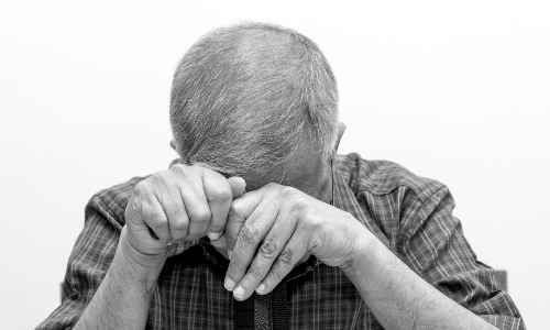 An older man, hiding his face with his hands